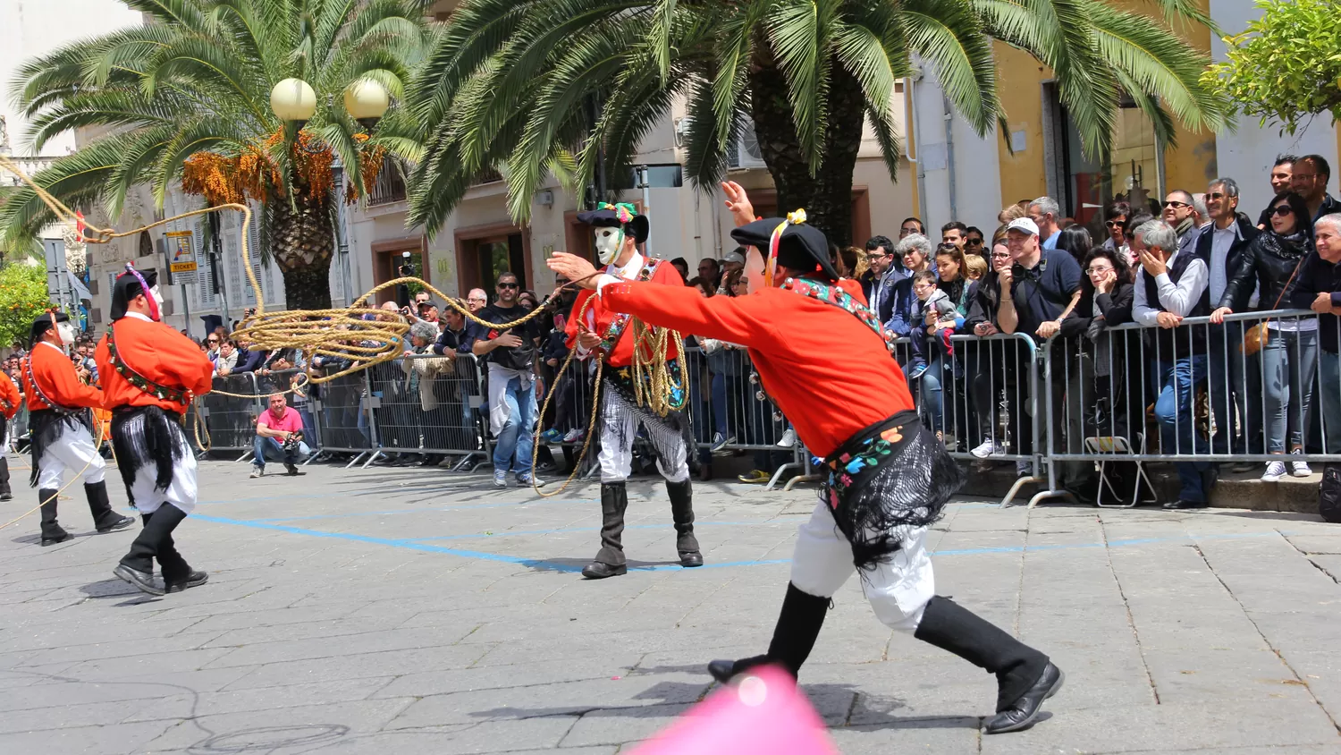 Un Issohadore con la giubba rossa lancia la fune durante la sfilata, fra la gente lungo le transenne