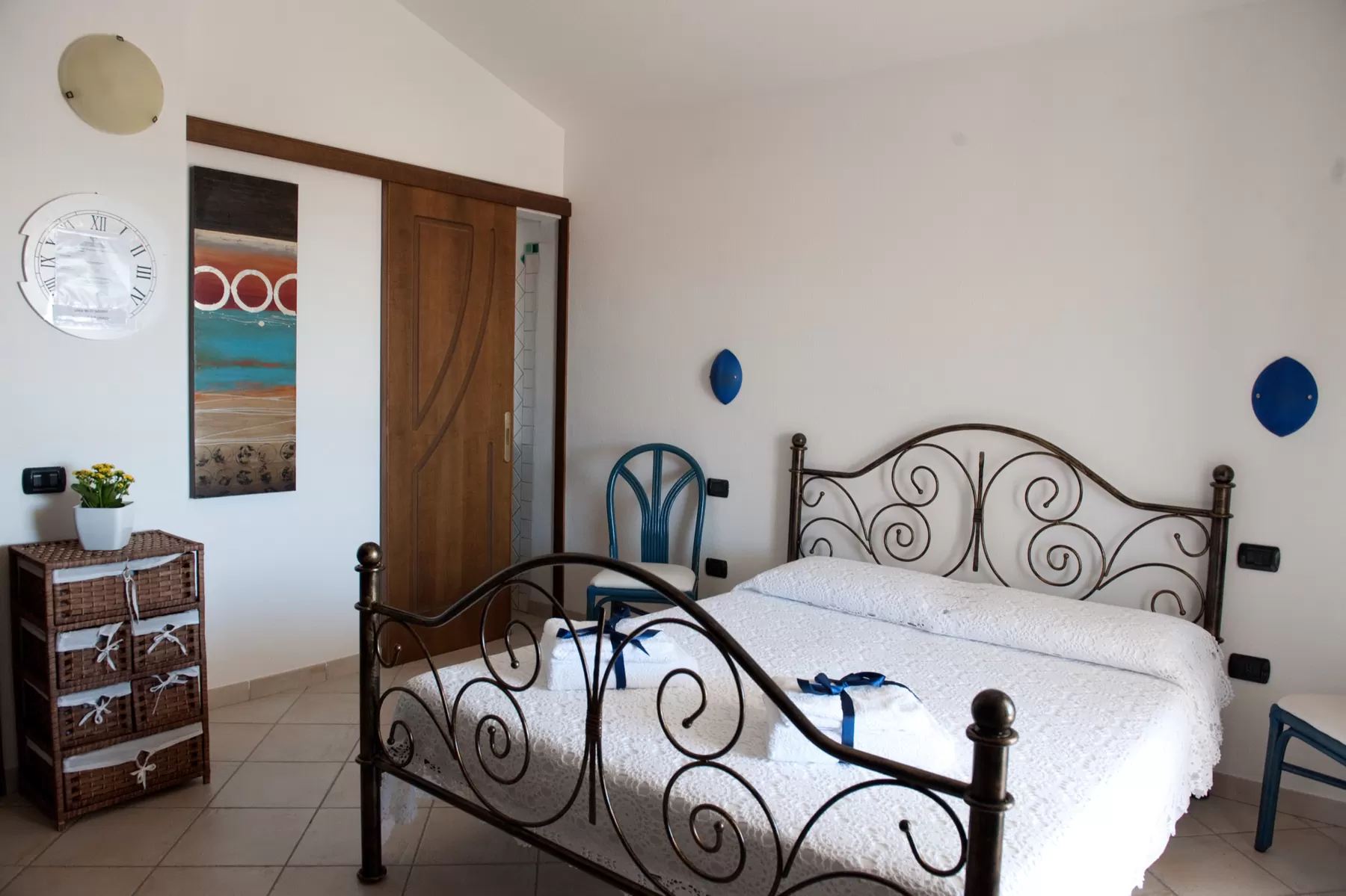 Camera con letto matrimoniale in ferro battuto a volute, due dischi di ceramica blu alle pareti e un quadro dai toni del mare
