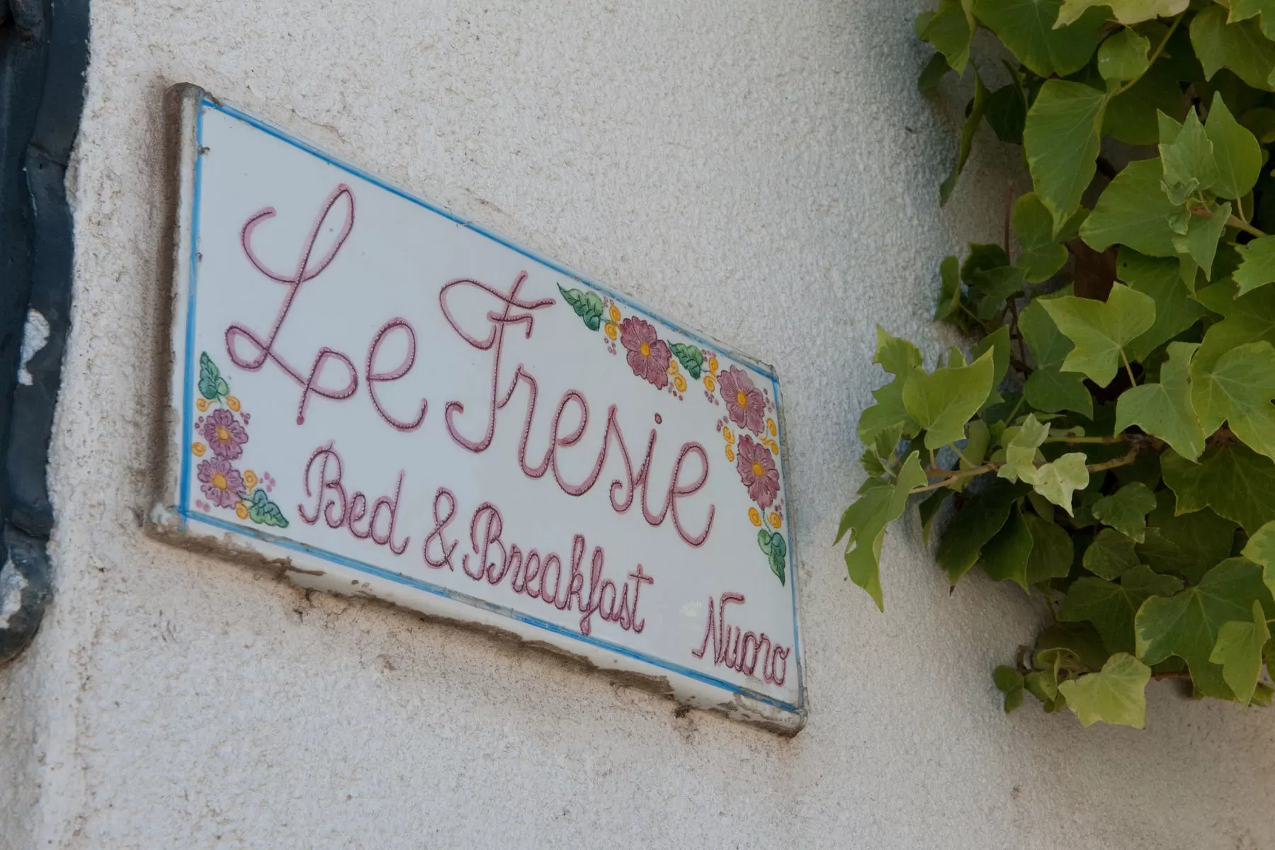 L'insegna in ceramica dipinta a mano con la scritta Le Fresie Bed & Breakfast Nuoro, accanto all'edera