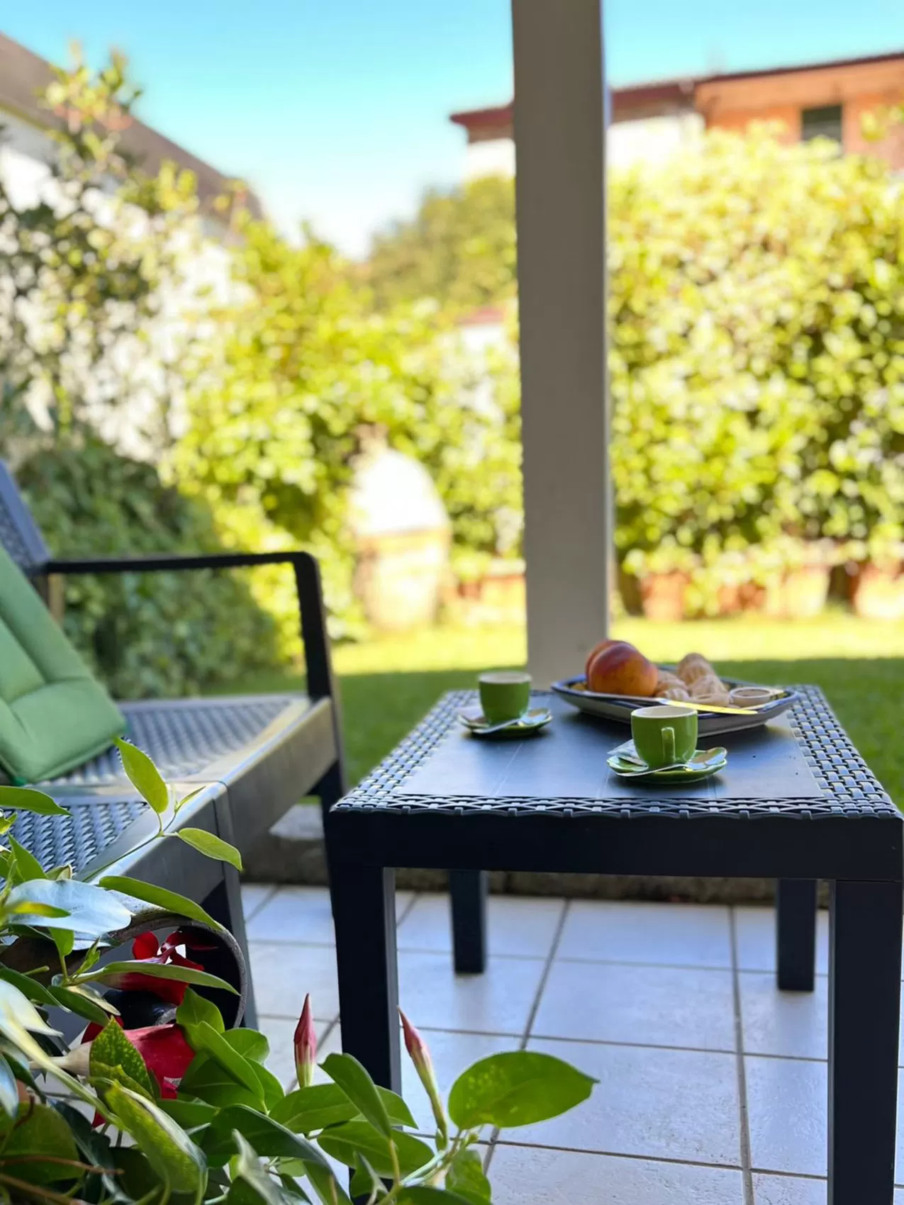 Il portico con le sdraio e il tavolino apparecchiato con caffè e frutta, affacciato sul prato del giardino