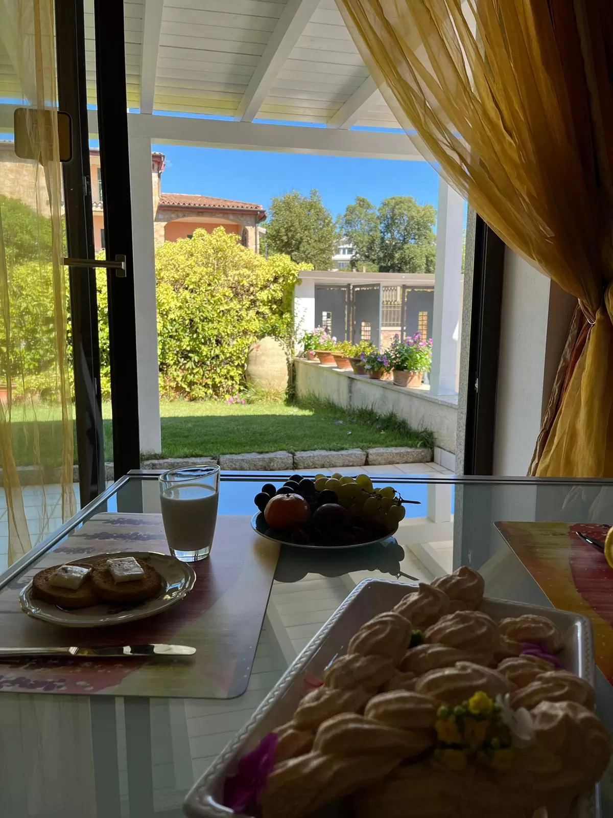 La tavola della colazione davanti alla vetrata aperta sul portico e sul prato del giardino