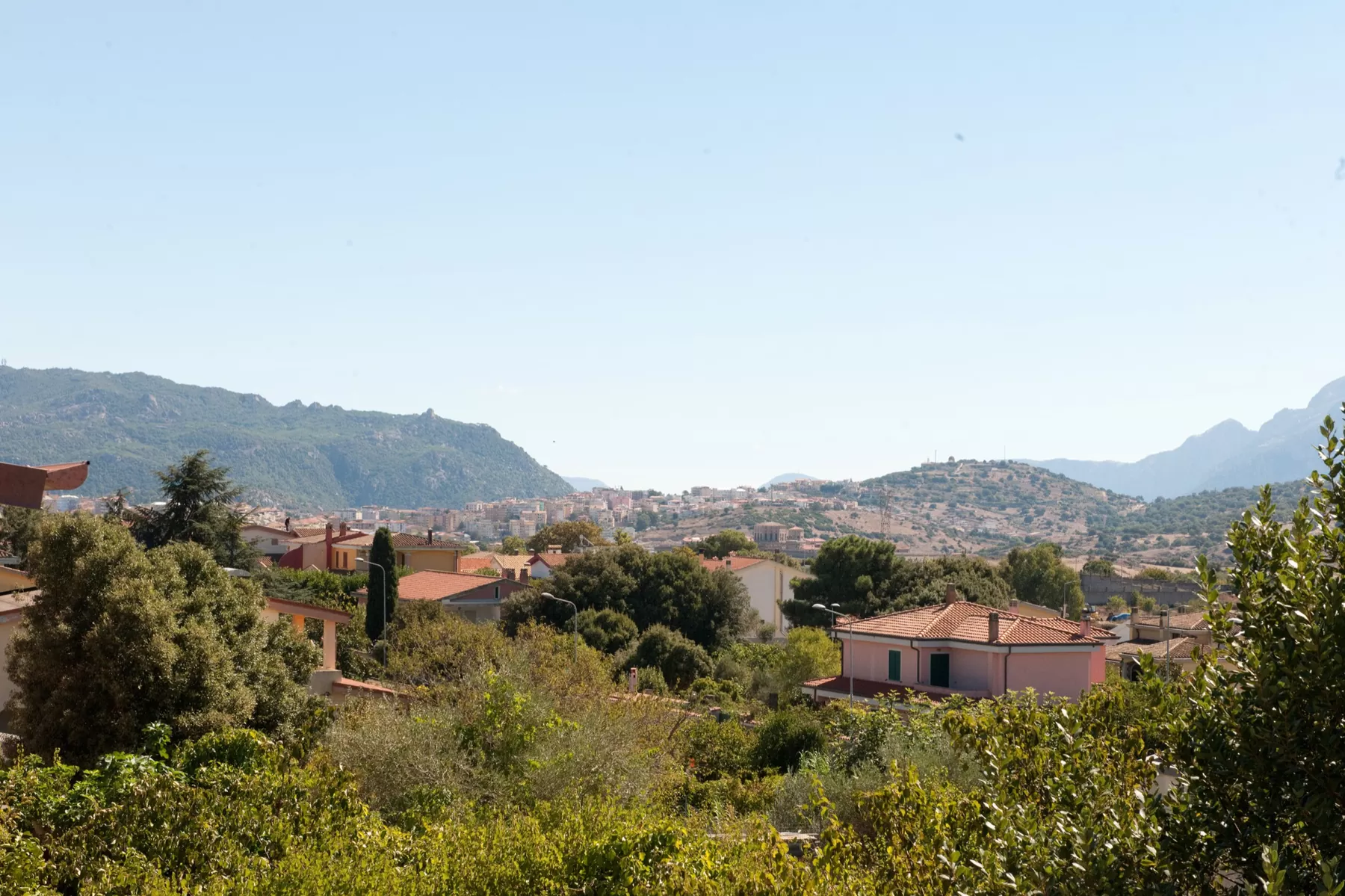 La vista dal balcone: i tetti del quartiere fra gli alberi, Nuoro sul crinale e le montagne del Supramonte sullo sfondo